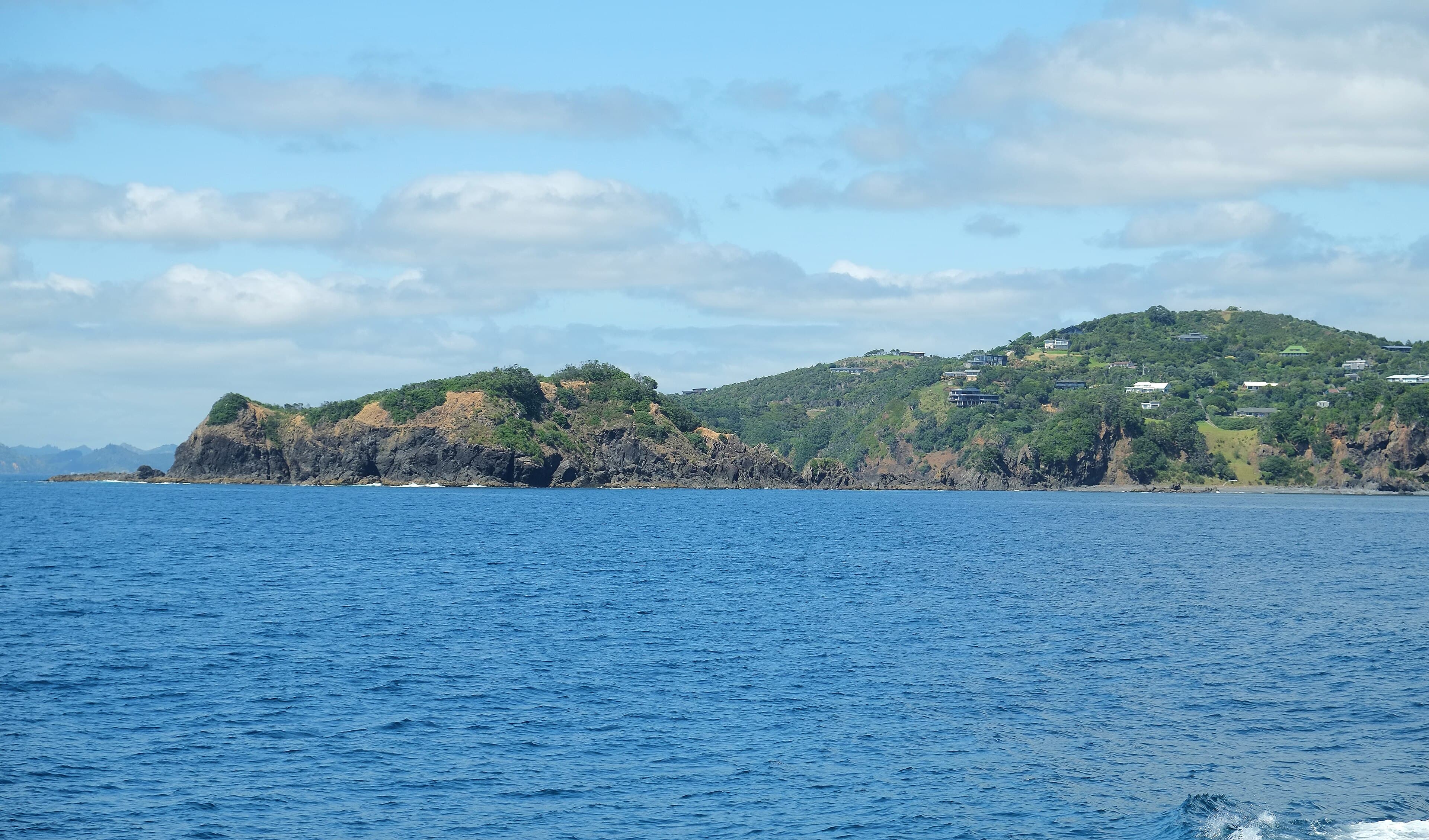 Rocky, green shoreline of Rahomaunu Island off the Tutukaka coast, viewed across blue water